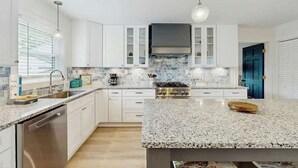 A modern kitchen with white cabinets, a granite countertop, a built-in stove, and a hanging light fixture. - Cherry Grove Beach Retreat (North Myrtle Beach)