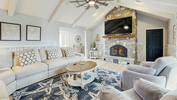 A living room with a stone fireplace, a ceiling fan, and a large TV mounted above it. - Cherry Grove Beach Retreat (North Myrtle Beach)