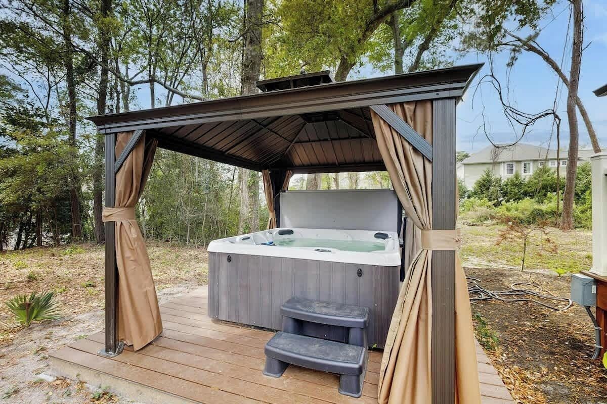 Ein Whirlpool unter einer Holz-Pergola mit einer Holzdielen-Terrasse und Stufen, die hinaufführen.