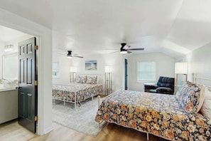 Ein Schlafzimmer mit zwei Betten, einem Sessel, Deckenventilatoren und einem Fenster mit Jalousien.