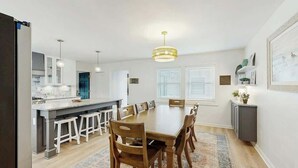 A modern kitchen with a central island, white cabinetry, and a dining area with a wooden table and chairs. - Cherry Grove Beach Retreat (North Myrtle Beach)