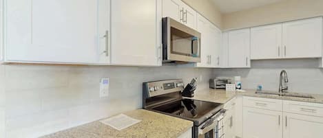 Una cocina con armarios blancos, encimera de granito, microondas, estufa y lavabo.