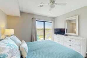 A bedroom with a bed, a TV, a dresser, and a sliding glass door leading to an outdoor area. - Tides Unit C-1 Condo (North Myrtle Beach)