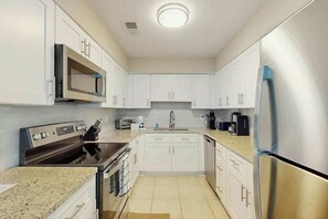 A modern kitchen with white cabinets, stainless steel appliances, and a granite countertop. - Tides Unit C-1 Condo (North Myrtle Beach)