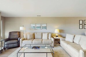 A living room with a sofa, armchairs, a coffee table, and two lamps. - Tides Unit C-1 Condo (North Myrtle Beach)