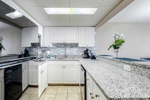 A modern kitchen with white cabinets, a granite countertop, a built-in oven, and a backsplash. - Sand Dunes Resort 2647/2648 (Myrtle Beach)