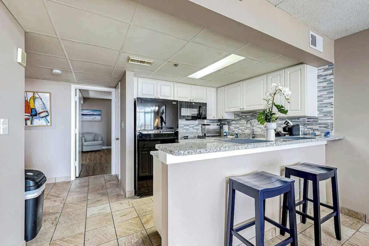 A modern kitchen with white cabinets, a granite countertop, and two bar stools.