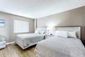 A hotel room with two beds, a nightstand, a lamp, a chair, and a window with blinds. - Sand Dunes Resort 2647/2648 (Myrtle Beach)