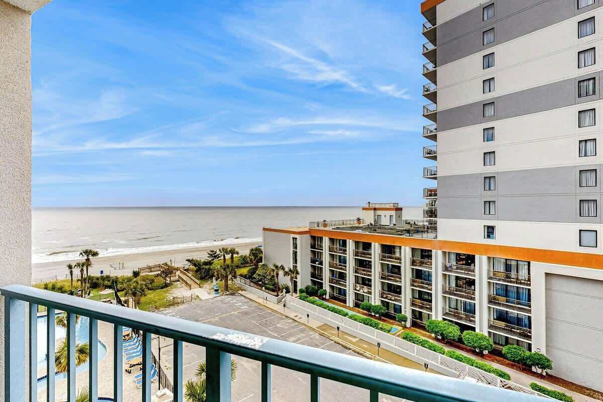 A hotel with a view of the beach, a pool, and a parking area.