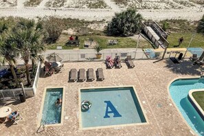 Ein Poolbereich mit zwei Pools, davon einer mit einem Buchstaben 'A' auf dem Boden, umgeben von Liegestühlen und einem kleinen Tisch.