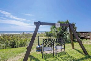 Spielplatz mit Schaukeln, einem Schild für Raucher, zwei Metallstühlen und Blick auf den Strand.