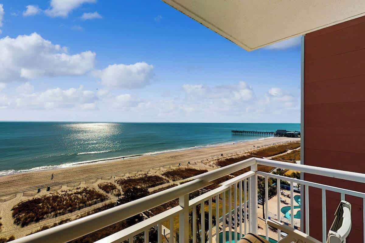 Un balcón con vista a una playa, un muelle y una zona de piscina.