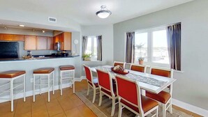 A modern kitchen with a dining area, featuring a central island, bar stools, and a table with chairs. - Bahama Sands Unit 0502 (North Myrtle Beach)