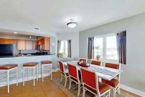 A modern kitchen with a dining area, featuring a central island, bar stools, and a table with chairs. - Bahama Sands Unit 0502 (North Myrtle Beach)