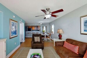 Ein Wohnzimmer mit Deckenventilator, braunem Ledersofa, Couchtisch und Essbereich im Hintergrund.