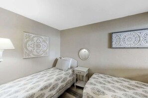 A bedroom with two beds, a bedside table, a mirror, and decorative wall art. - Sands Ocean Club 1629/1630 (Myrtle Beach)