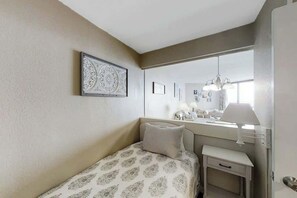 A bedroom with a bed, bedside table, lamp, and a mirror reflecting a window. - Sands Ocean Club 1629/1630 (Myrtle Beach)