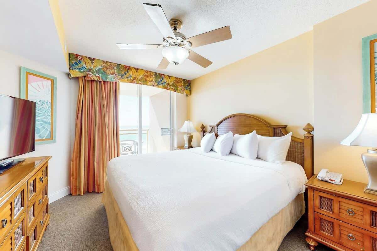 Een hotelkamer met een bed, een plafondventilator, een houten dressoir en een televisie.