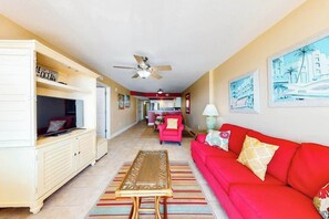 A living room with a red sofa, a television on a cabinet, and a ceiling fan. - Bahama Sands Unit 0506 (North Myrtle Beach)