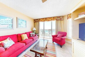 A living room with a red sofa, a glass coffee table, and a red armchair. There is a balcony with a view. - Bahama Sands Unit 0506 (North Myrtle Beach)