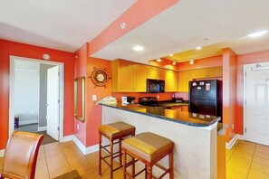 A kitchen with a central island, wooden stools, and a refrigerator. - Bahama Sands Unit 1201 (North Myrtle Beach)