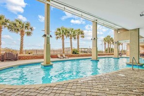 An indoor swimming pool with clear blue water, surrounded by palm trees and a covered area with lounge chairs. - Bahama Sands Unit 1201 (North Myrtle Beach)