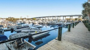 A marina with boats docked, a wooden walkway, and a bridge in the background. - Harbourgate Unit 0412 (North Myrtle Beach)