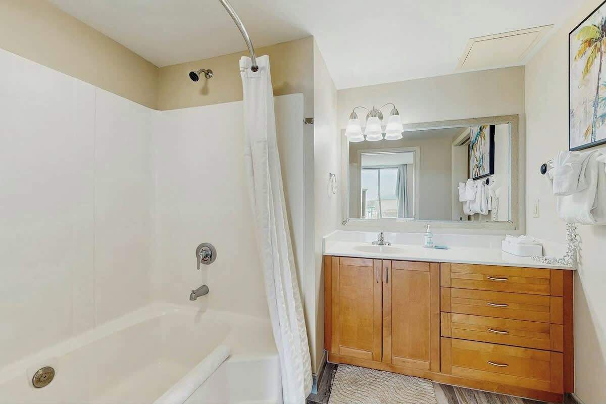 A modern bathroom with a bathtub, a shower curtain, a vanity with a mirror, and wooden cabinets.