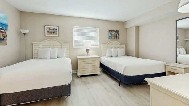 A hotel room with two beds, a bedside table with a lamp, a dresser, and a large mirror. - Harbourgate Unit 0412 (North Myrtle Beach)