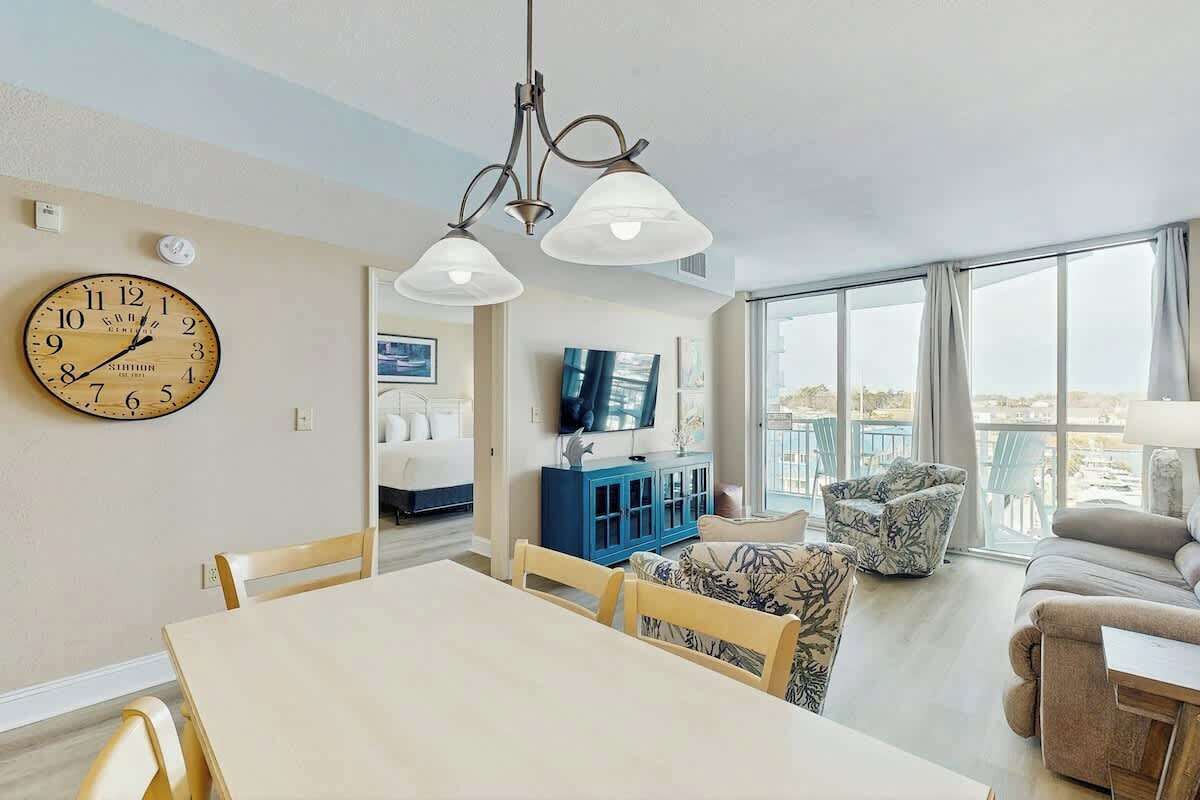 A spacious living area with a dining table, sofas, a TV, and a large window offering a view.