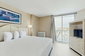 Ein Hotelzimmer mit einem großen Bett, einem Fernseher, einem Schreibtisch und einem Fenster mit Blick auf die Stadt.
