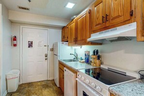 A compact kitchen with wooden cabinets, a white stove, a dishwasher, and a sink. - La Mirage Unit 302 Condo (Myrtle Beach)