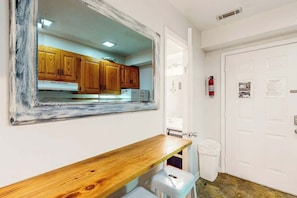 A room with a wooden bench, a white door, and a kitchen area visible through a mirror. - La Mirage Unit 302 Condo (Myrtle Beach)