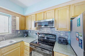 A kitchen with wooden cabinets, a stainless steel microwave, a stove, and a refrigerator. - Crescent Towers I - 304 (North Myrtle Beach)