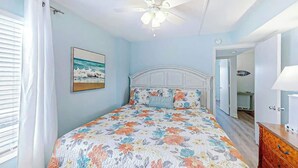 A bedroom with a bed, a ceiling fan, a painting, and a door leading to another room. - Crescent Towers I - 304 (North Myrtle Beach)