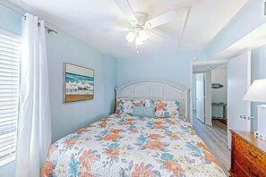 A bedroom with a bed, a ceiling fan, a painting, and a door leading to another room. - Crescent Towers I - 304 (North Myrtle Beach)