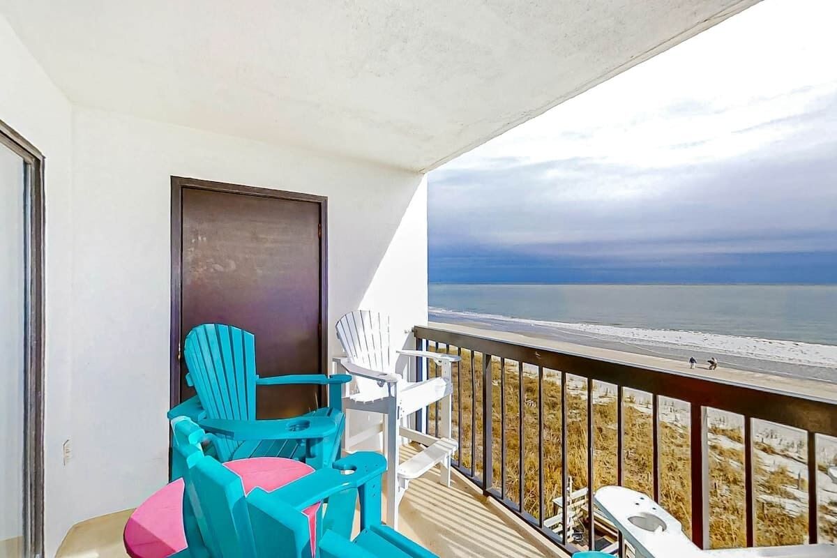 A balcony with a view of the beach, a door, and two chairs.