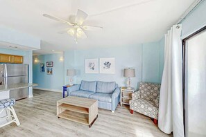 A modern living room with a sofa, coffee table, patterned armchair, and a ceiling fan. - Crescent Towers I - 304 (North Myrtle Beach)
