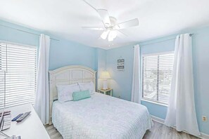 Een slaapkamer met een bed, nachtkastje, lamp en plafondventilator.