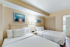 A hotel room with two beds, a nightstand with a lamp, and a painting on the wall. - Camelot by the Sea 0501 (Myrtle Beach)