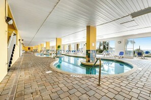 Ein Innenpool mit gefliestem Boden, Liegestühlen und freiem Blick ins Freie.