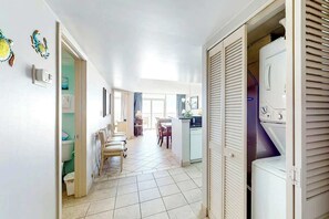 Un couloir mène à une cuisine équipée d’un lave-linge, à un coin repas avec des chaises, et offre une vue sur la salle de bain.