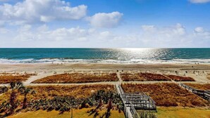 Una platja amb cel clar, sorra daurada i un passeig marítim que condueix a l'aigua.