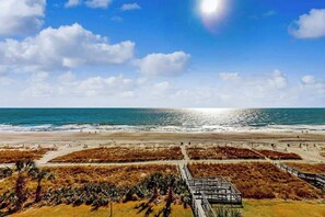 Ein Strand mit blauem Himmel, sandigem Ufer und einer Promenade, die zum Wasser führt.