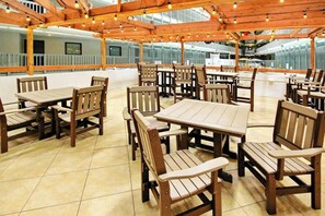 Ein Restaurant mit Holztischen und -stühlen, einem Fliesenboden und Blick auf ein Gebäude durch große Fenster.