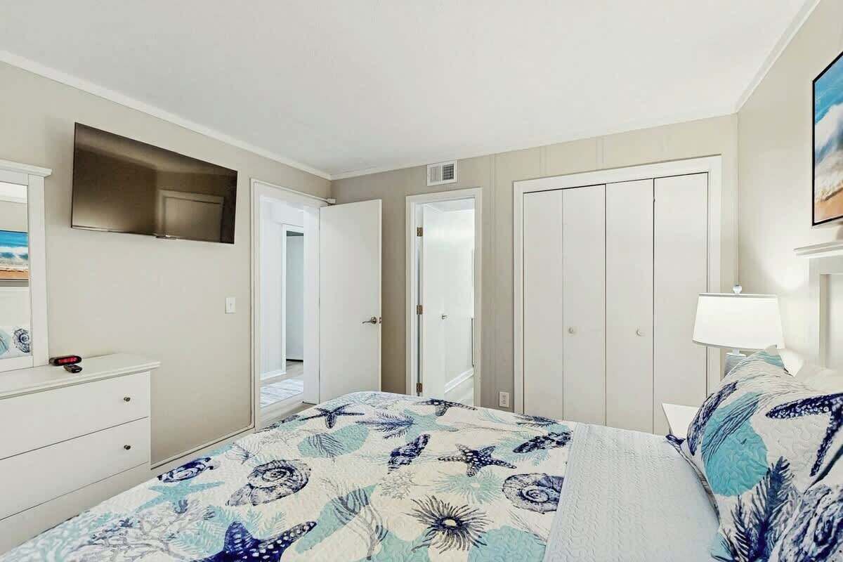 Ein Schlafzimmer mit Bett, Kommode, Spiegel, Fernseher und einer Tür.