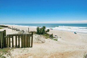 Ein Strand mit Holzzaun, sandigem Untergrund und blauem Himmel.