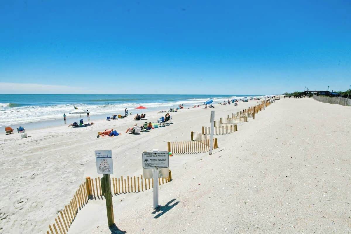 A beach with a wooden fence, beachgoers, and a clear sky.