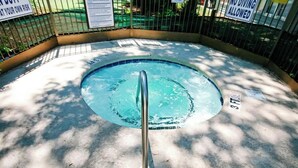 A circular pool with a metal pole in the center, surrounded by a concrete deck and a metal fence.