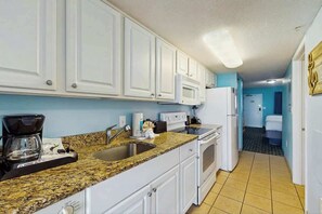 A kitchen with white cabinets, a granite countertop, a coffee maker, a microwave, and a refrigerator. - Paradise Resort 1005 (Myrtle Beach)